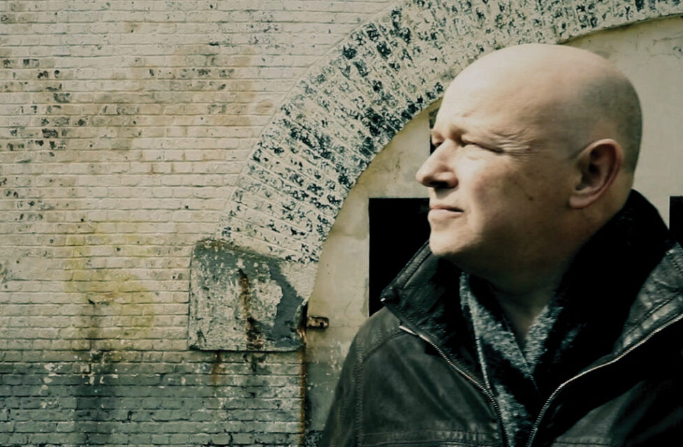 A man stands in front of a building looking away from the camera